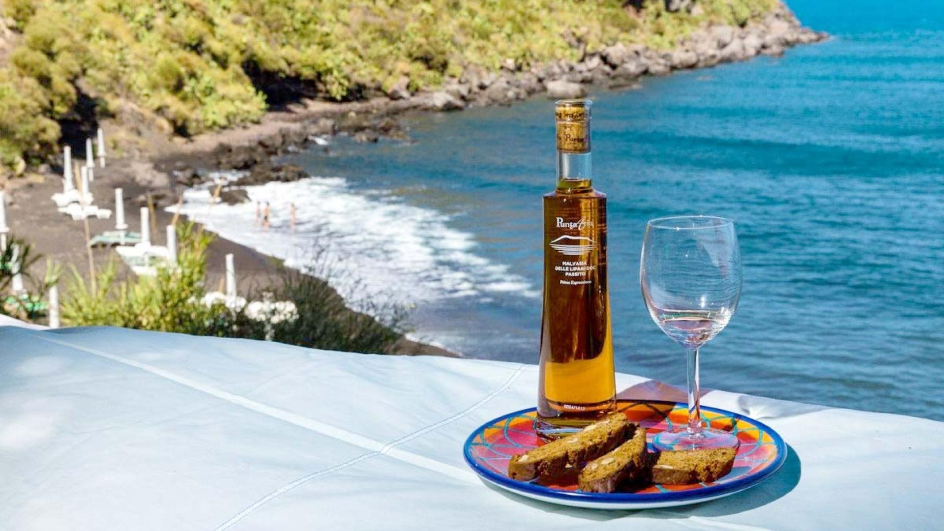 Bottiglia di vino e pane su tavolo, vista mare e spiaggia soleggiata.