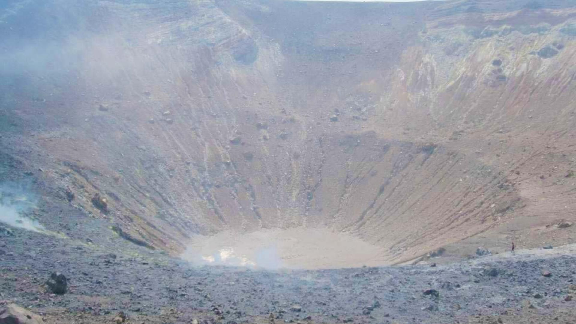 Un cratere vulcanico arido, avvolto da fumo, emana un'atmosfera di desolazione e maestosità.