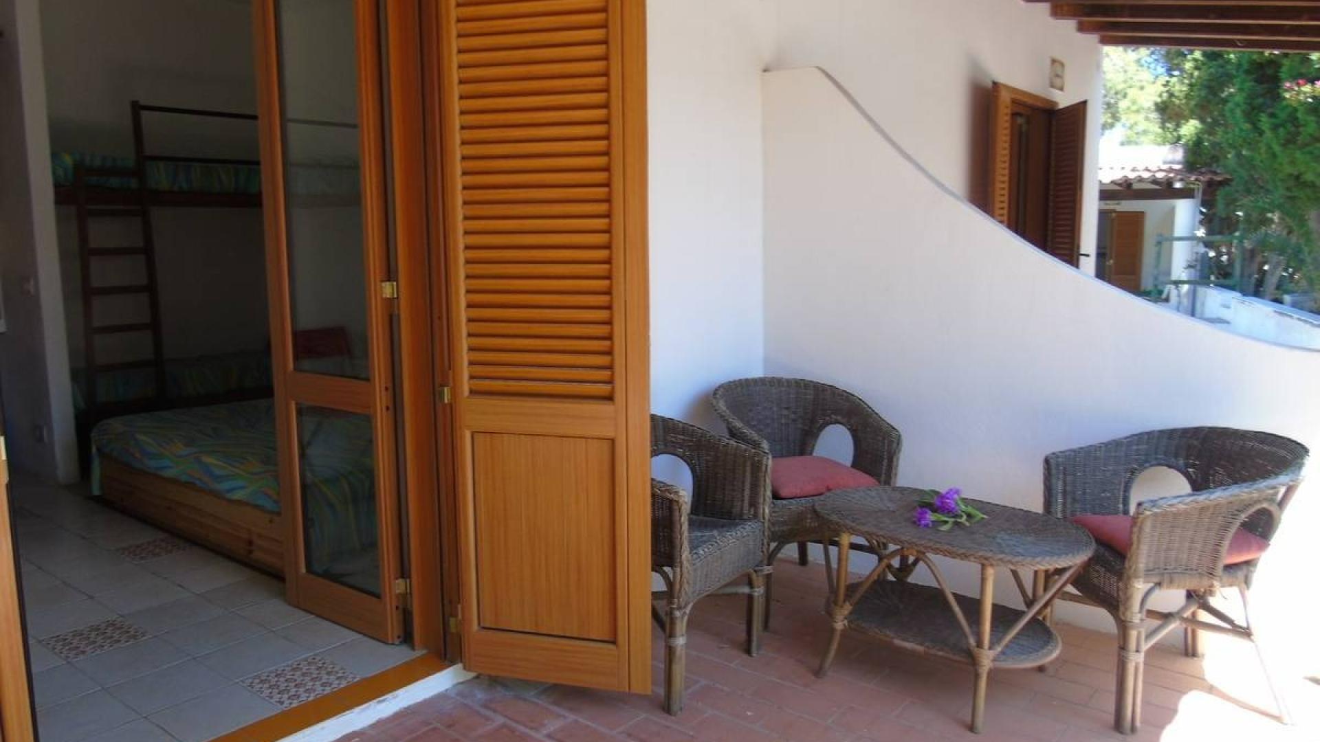 Terrazza accogliente con sedie in vimini, tavolino e vista su una camera luminosa.