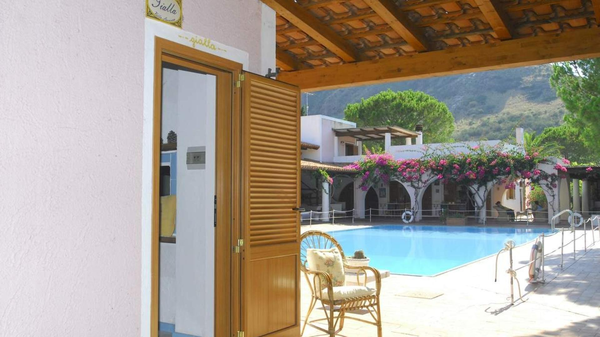 Piscina luminosa, fiori colorati, sedia accogliente, atmosfera rilassante e vista montuosa.