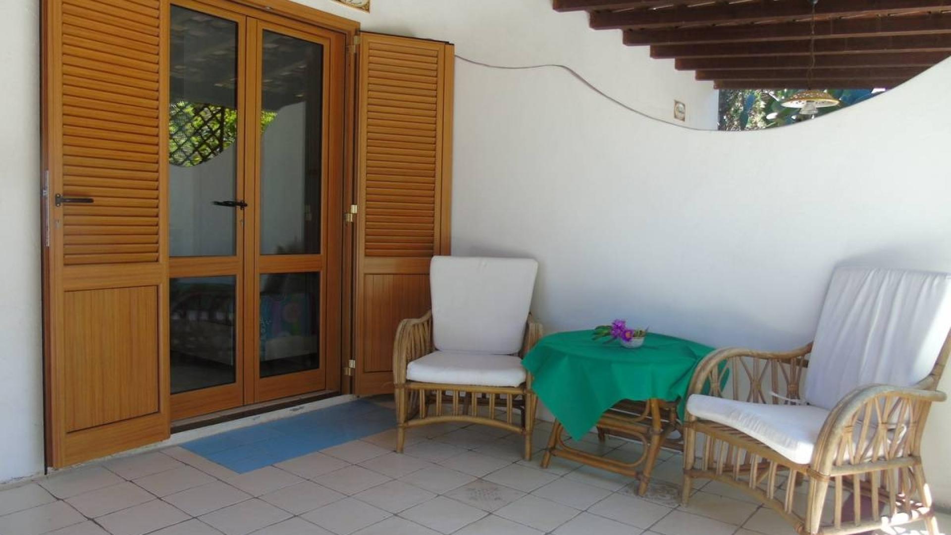 Veranda accogliente con sedie in vimini, tavolo verde e atmosfera rilassante.