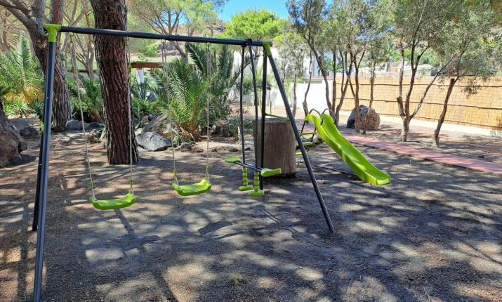 Altalene e scivolo verde in un parco ombreggiato, atmosfera rilassante e naturale.