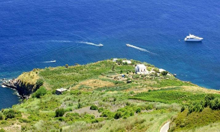 Vista aerea di un'isola verde, mare blu intenso, barca bianca, serenità assoluta.
