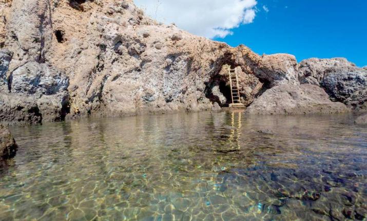 Scogliera con scala, acqua cristallina, cielo azzurro: un invito all'avventura e alla scoperta.
