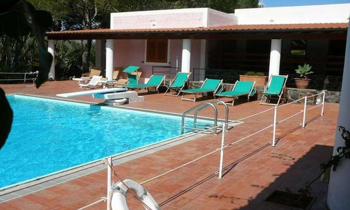 Piscina azzurra, sdraio verdi, terrazza soleggiata: relax estivo in una villa tranquilla.