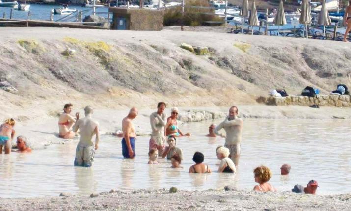 Persone rilassate in una pozza termale, immerse nel fango, atmosfera di benessere e tranquillità.