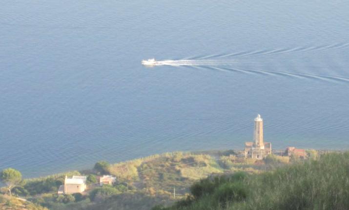 Faro solitario sorveglia il mare calmo, mentre una barca lascia una scia serena.