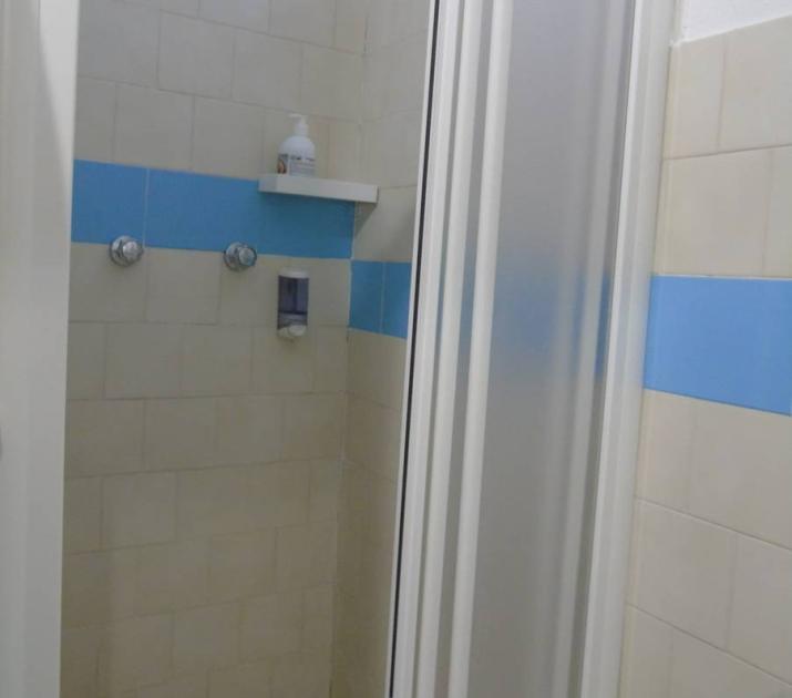 Doccia semplice, piastrelle beige e blu, atmosfera pulita e ordinata, luce soffusa.
