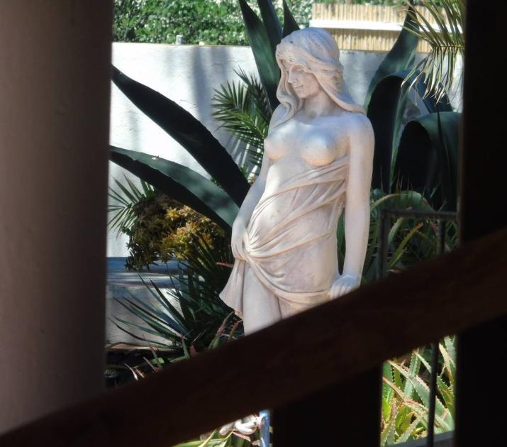 Statua di donna avvolta in drappeggio, circondata da piante esotiche, atmosfera tranquilla.