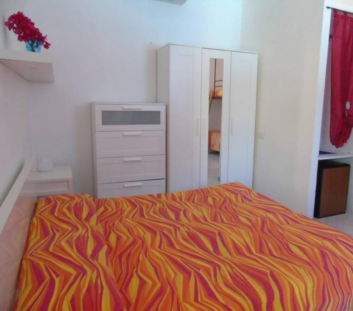 Camera accogliente con letto colorato, mobili bianchi e bagno annesso, atmosfera vivace e luminosa.