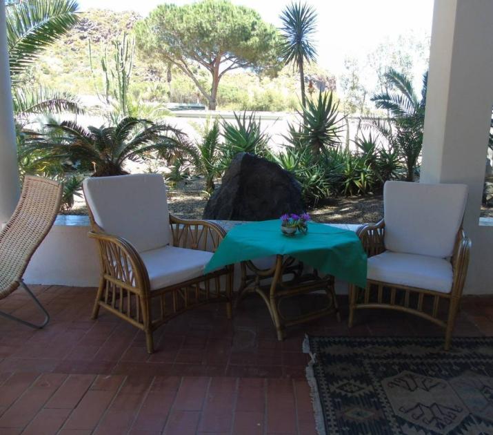 Veranda accogliente con sedie in vimini, tavolo verde e piante rigogliose all'aperto.
