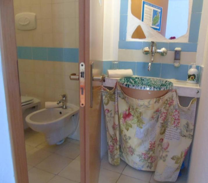 Bagno rustico con lavabo decorato e tenda floreale, atmosfera accogliente e vintage.