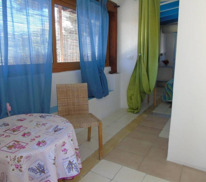 Interno accogliente con tende colorate, tavolo fiorito e atmosfera luminosa e serena.