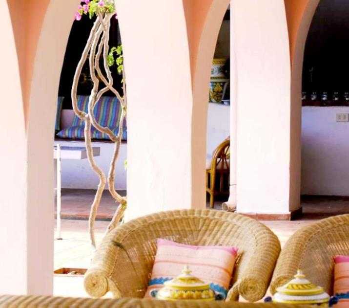 Architettura mediterranea con archi rosa, sedie di vimini e dettagli decorativi evocano relax e calore.