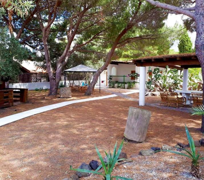 Giardino ombreggiato con pini, gazebo e sedie in legno, atmosfera serena e accogliente.