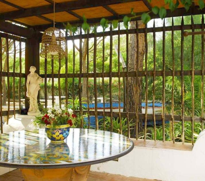Giardino sereno, tavolo colorato, statua elegante, natura rigogliosa, atmosfera accogliente e rilassante.