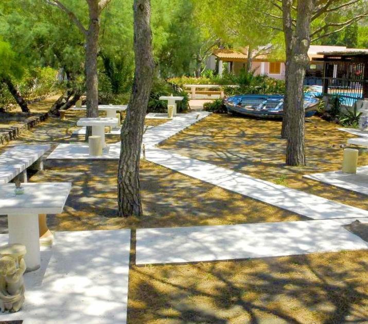 Giardino ombreggiato con tavoli bianchi, pini e atmosfera serena, ideale per relax all'aperto.
