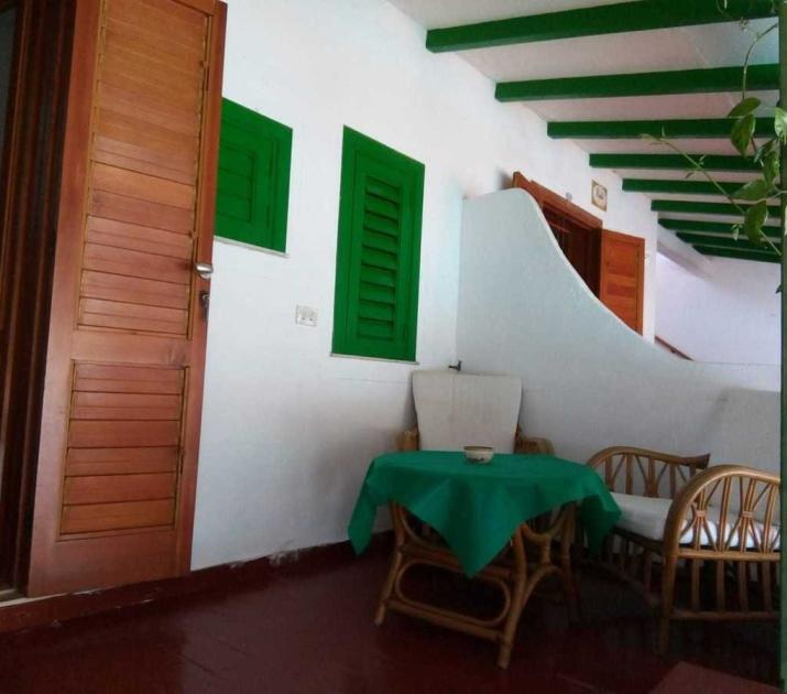 Veranda accogliente con sedie in rattan, tavolo verde e atmosfera rilassante.