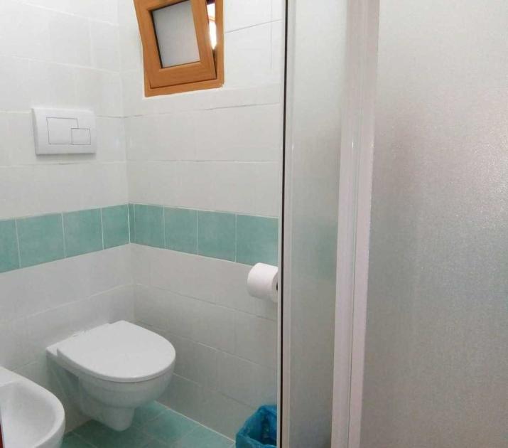 Bagno moderno, pulito e luminoso, con piastrelle verde acqua e finestra in legno.