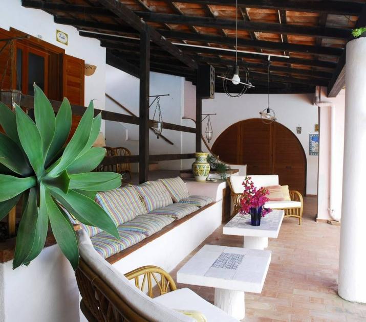 Terrazza accogliente con piante verdi, sedute colorate e tavoli bianchi, atmosfera mediterranea rilassante.