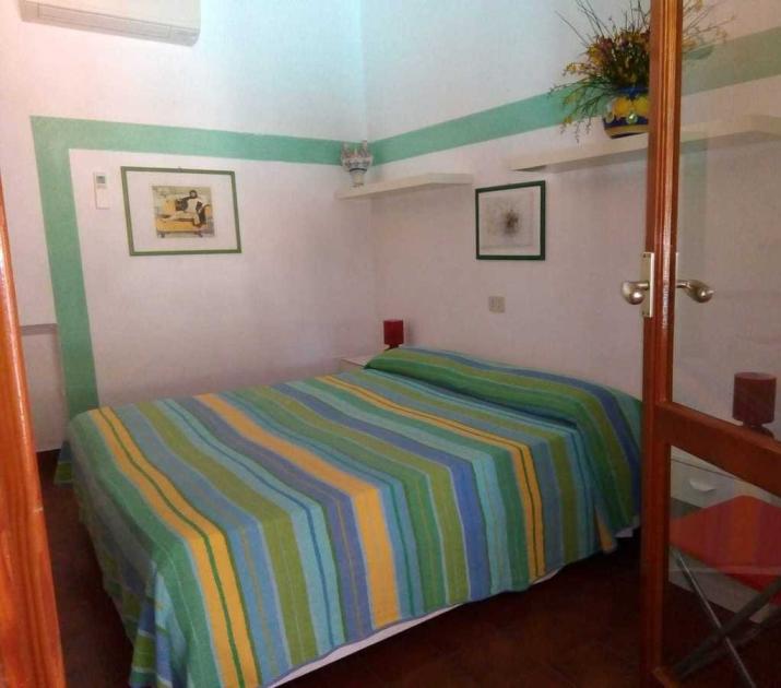 Camera accogliente, letto colorato, quadri alle pareti, atmosfera tranquilla e rilassante.