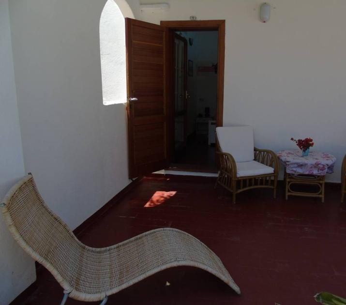 Terrazza accogliente con sedie di vimini, tavolino fiorito, luce solare calda e rilassante.