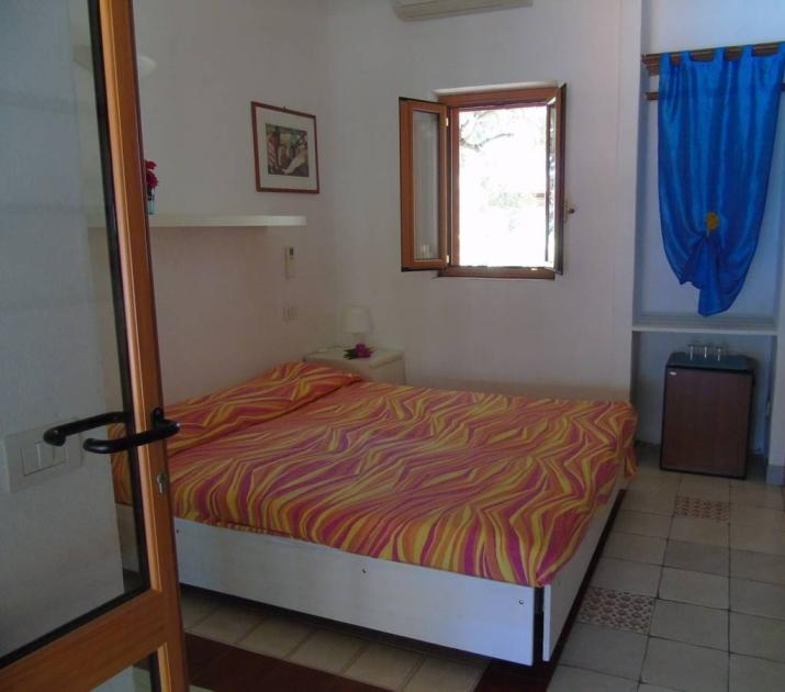 Camera accogliente con letto colorato, finestra aperta e tenda blu vivace.