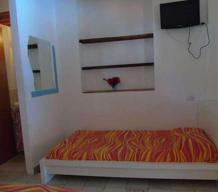 Stanza accogliente, letto vivace, specchio ondulato, TV, mensole e fiori aggiungono calore.