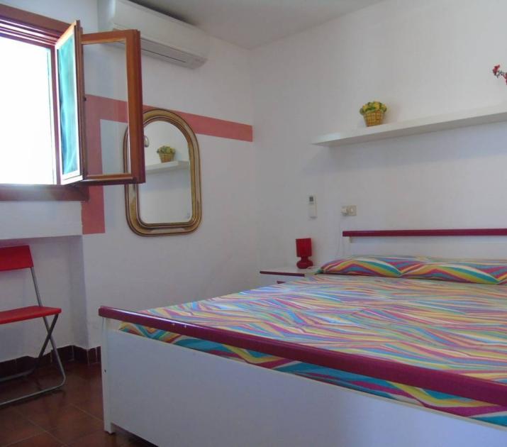 Camera luminosa con letto colorato, arredi semplici e atmosfera accogliente.
