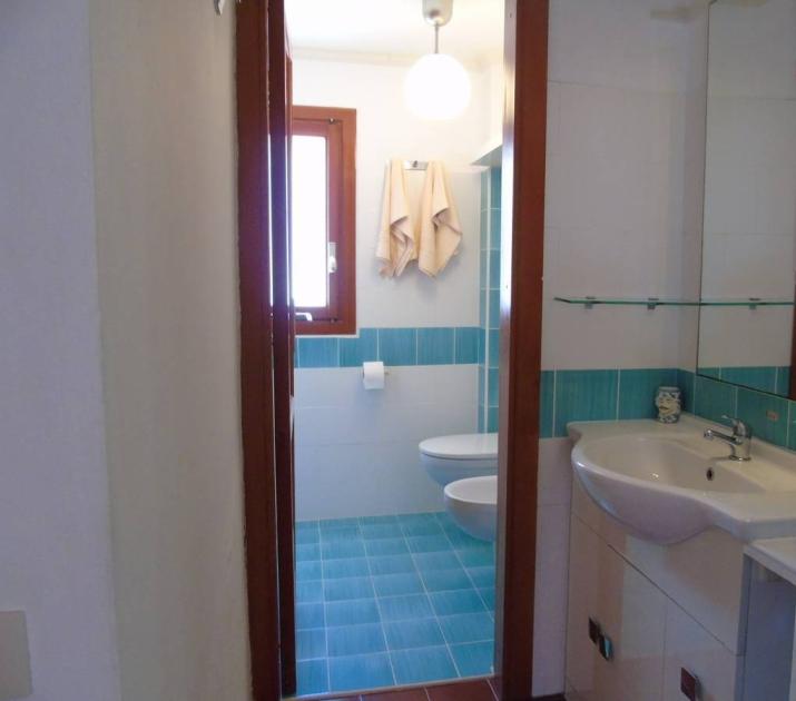 Bagno luminoso con piastrelle azzurre, lavabo bianco e asciugamani appesi.