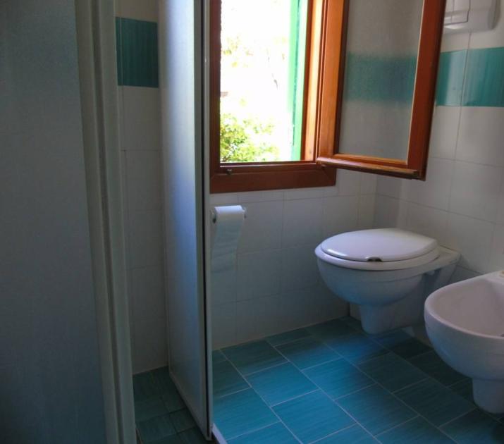 Bagno luminoso con piastrelle turchesi, finestra aperta, atmosfera fresca e accogliente.