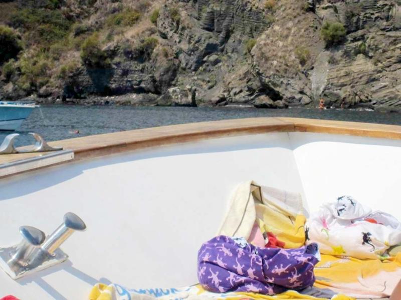 Barca al sole, teli colorati, mare calmo, scogliere selvagge. Atmosfera estiva e rilassante.
