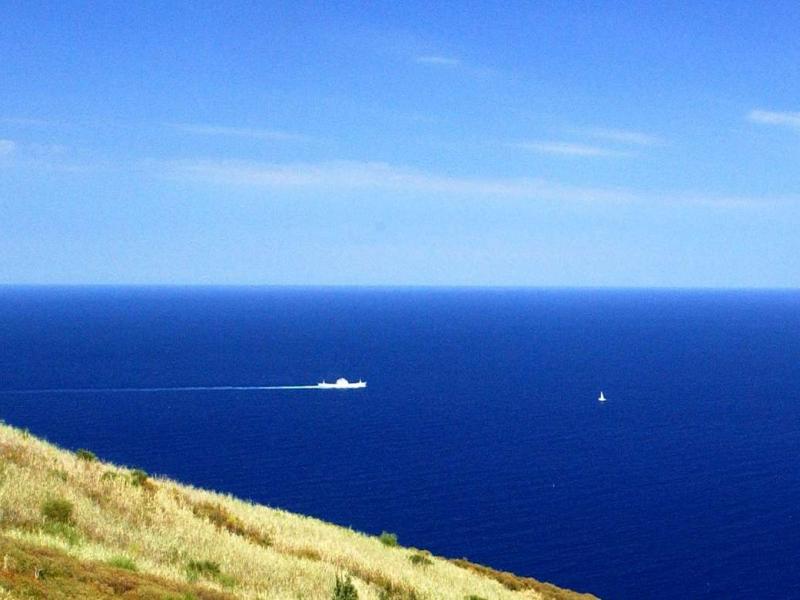 Mare blu infinito, barca bianca lontana, pace e libertà sotto un cielo sereno.