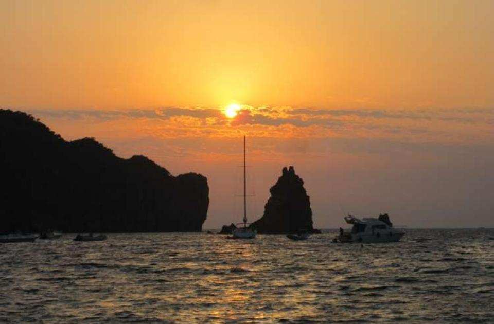 Tramonto dorato sul mare, barche silenziose e ombre di scogliere maestose.